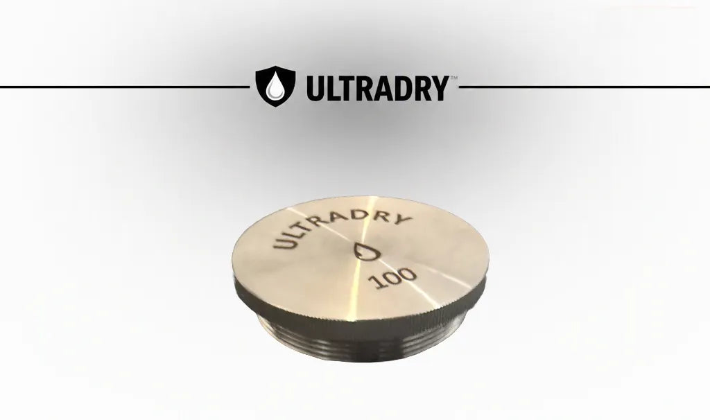 An ULTRADRY 100 gram stainless steel desiccant cartridge lid, shown at an angle on a light gray gradient background with the ULTRADRY brand logo and text at the top.