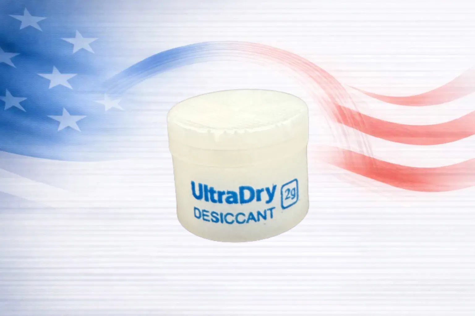 A small white plastic jar of UltraDry Desiccant 2 grams, featuring blue text, set against a stylized American flag background with red and white stripes and blue stars.