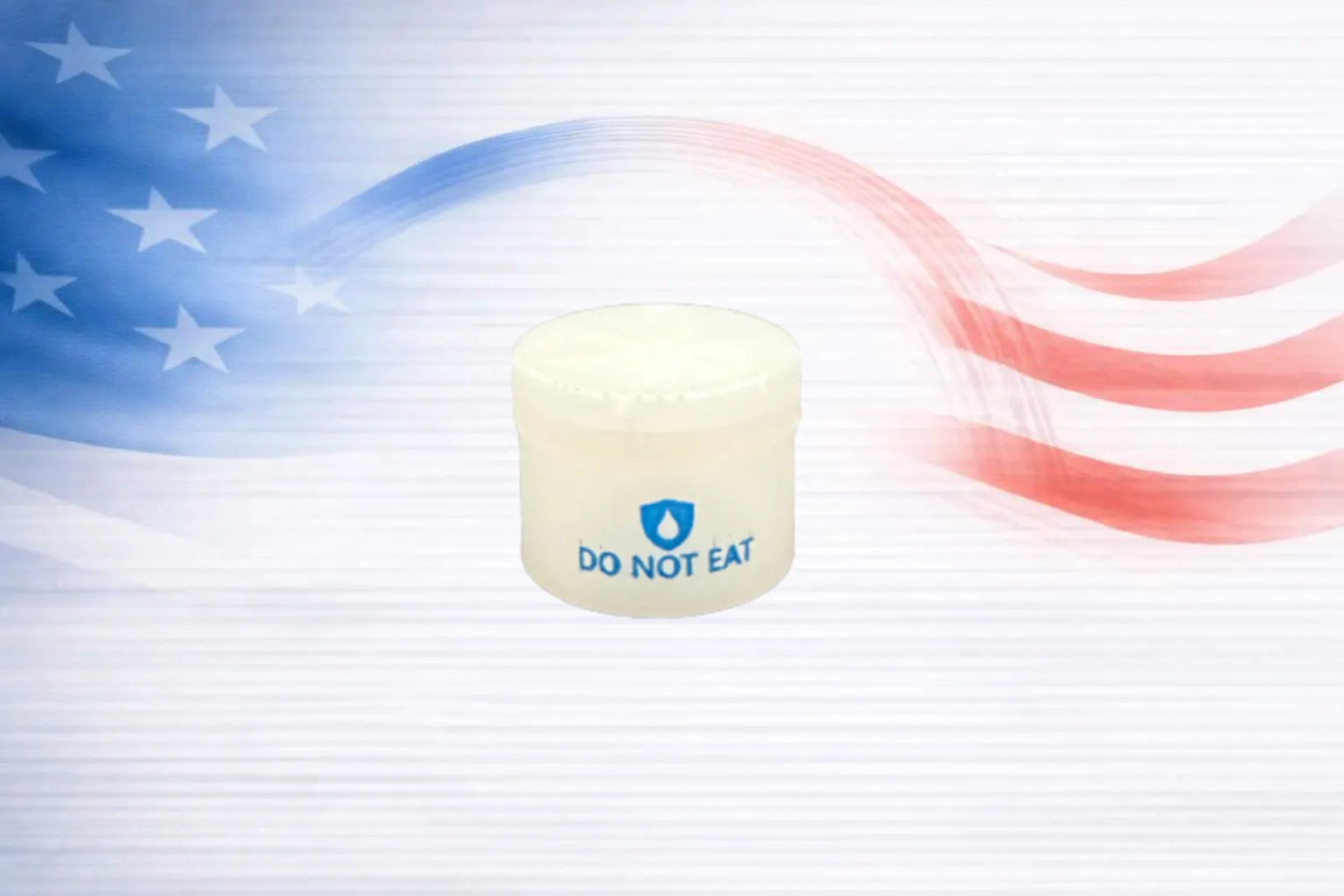 A small white plastic 2 gram silica desiccate jar with a white lid, featuring a blue ultradry shield logo and the text 'DO NOT EAT' on the back. The jar is centered against a stylized background with a blue and red American flag motif on a white striped base.