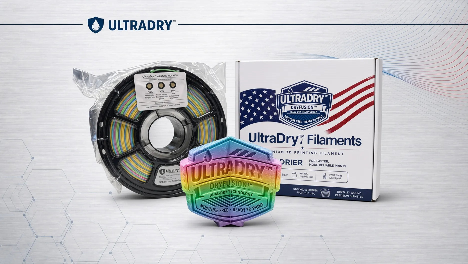 Ultradry Filaments 3D printing filament spool, packag d in its vacuum seal bag and showing a dry humidity indicator sealed in the package, shown next to its retail box and a colorful Ultradry logo badge, on a light gray background with a subtle hexagonal pattern.